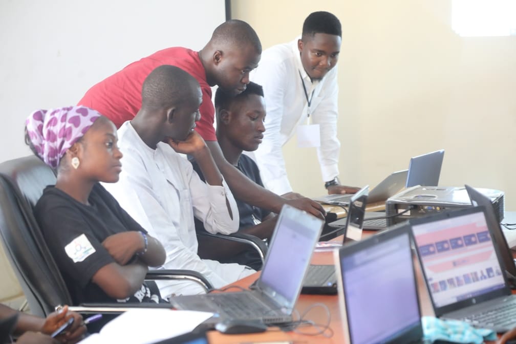 A Toko Academy instructor leaning over a learner's laptop while classmates follow along